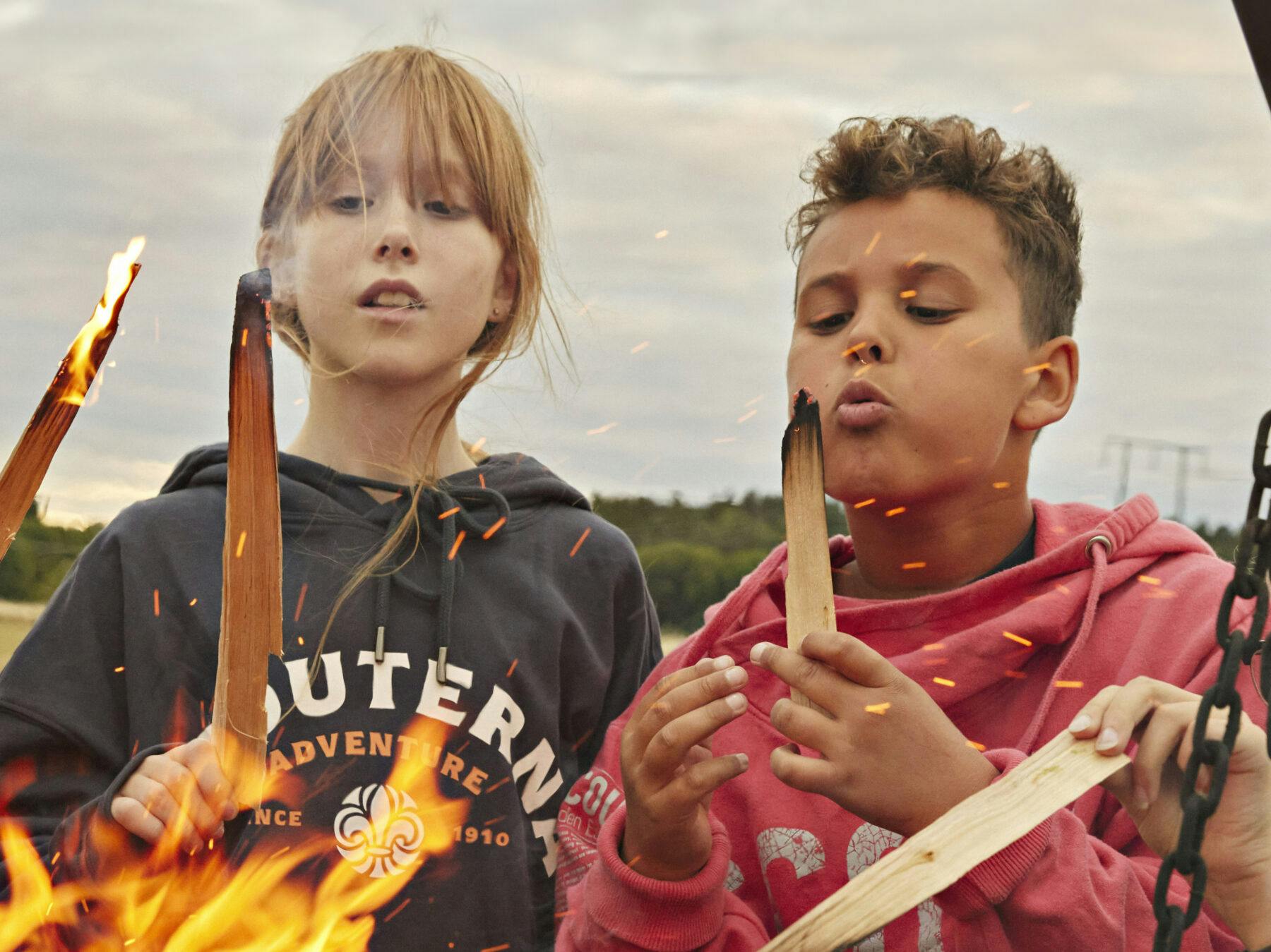 Två barn stoppar pinnar i elden.