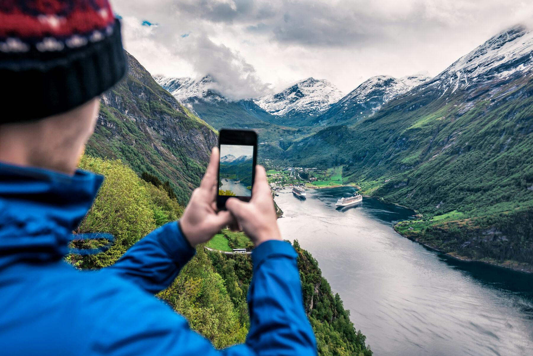 tourist takes photo of Geiranger fjord on smartphone in Norway
